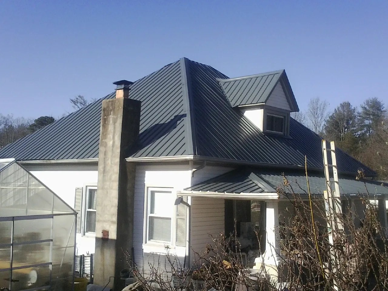 Dark blue standing seam metal roof on a white farmhouse with dormer — Slate & Tile Roof Repair by Roofing Brothers in Bulverde