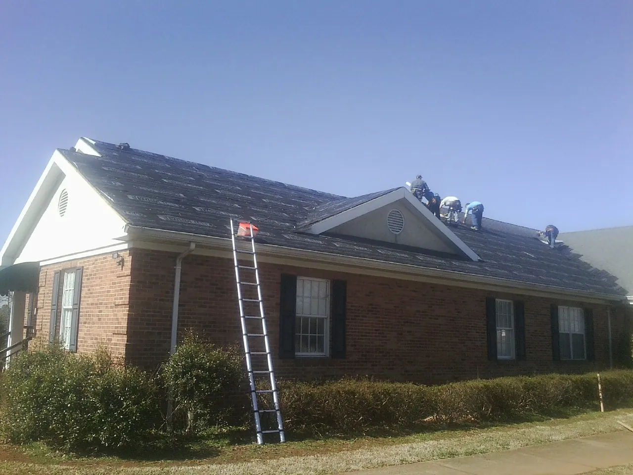 Crew tearing shingles off a brick ranch roof with a ladder set — Emergency Roof Repair work by our crew in Bulverde