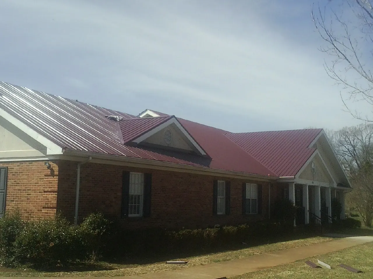 Red metal roof with gabled entries on a long brick building, from a Hail Damage Roof Repair job in Bulverde