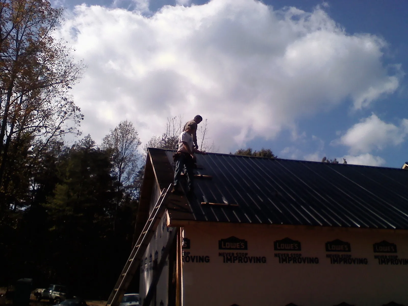 Roofer fastening dark metal panels high against a cloudy sky, from a Roof Inspection job in Bulverde